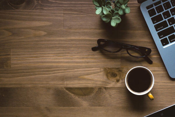 Schreibtisch mit Tasse, Brille und Laptop
