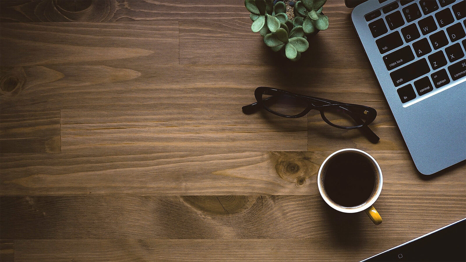 Schreibtisch mit Tasse, Brille und Laptop